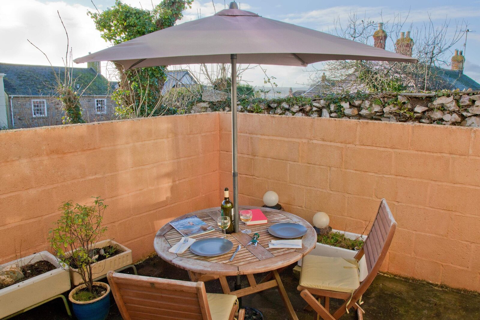 Enclosed sun-trap patio with table, parasol and pot plants